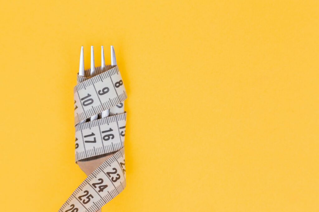 Weight loss measuring tape wrapped around a fork with yellow background