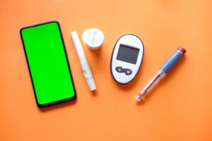 Collection of diabetic equipment and mobile phone on orange background